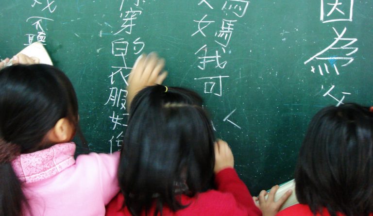 Chinese girls writing Chinese characters on a green board.