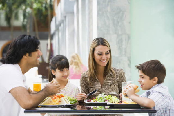 Family sits at a table in public, father with dark hair followed by a daughter, mother and a son.