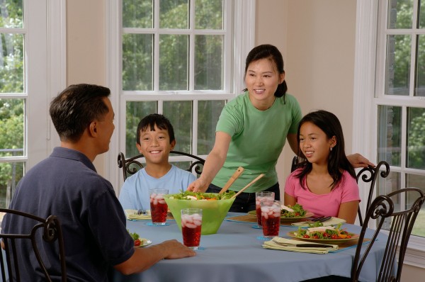 Asian Family at the table. Father two children and a mother reaching from inbetween the children passing the father a green salad bowl.