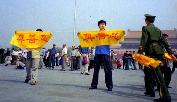 A Falun Gong practitioner holds a banner at Tiananmen Square reading “Truth, Compassion, Tolerance,” the core tenets of the practice. A policeman approaches to arrest him. (Image: Falun Dafa Information Center)