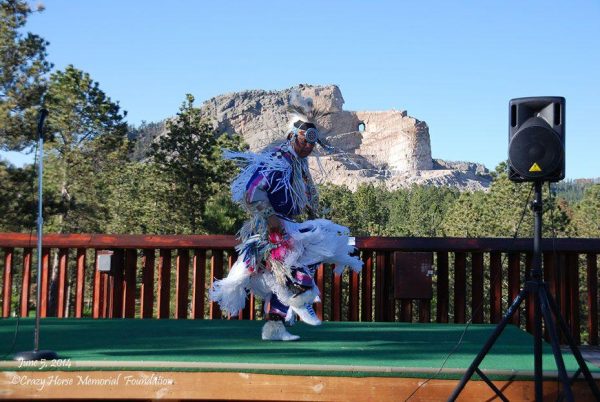 A Native American dancer, with the Crazy Horse Memorial in the distance. Korczak Ziolkowski and the Lakota tribal elders wanted the Crazy Horse Memorial to be more than a monument. Ziolkowski said, “Crazy Horse is not just a place; Crazy Horse is a living symbol.” The monument serves as a focal point for Native American culture. (Image: Crazy Horse Memorial Foundation)