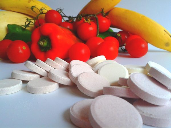 Fruits and Vegetables as a backdrop to meds and supplements on a white table.
