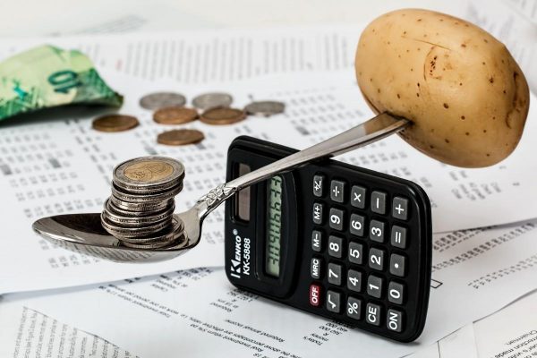 A potato balanced by coins over a calculator showing the importance to manage one's finances wisely.