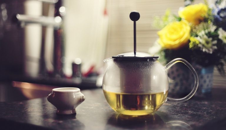 A pot of green tea sits on a table next to some yellow roses.