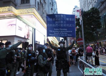 Hong Kong policeman holding a sign that says "Police Warning: This meeting or procession is in breach of the law. Disperse or we may use force."