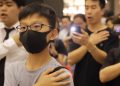 People in a shopping mall in Hong Kong stand with hands on hearts, singing "Glory to Hong Kong".