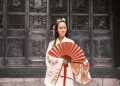 A Chinese girl wearing traditional clothing and carrying a fan.