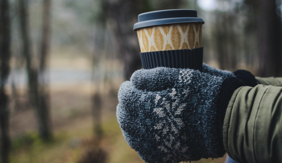 Closeup of someone holding an insulated cup in gloved hands.
