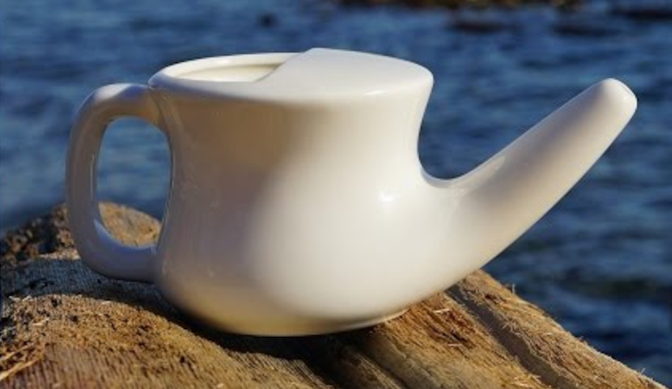 Close up of a white neti pot sitting on a rock by the ocean.