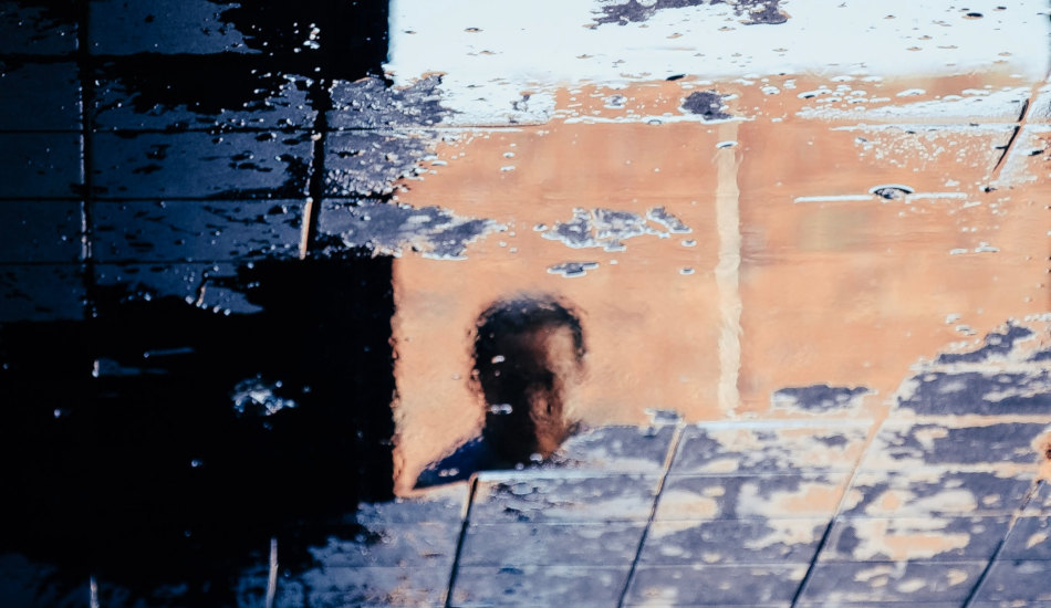 A man's face reflected in a puddle on the sidewalk.
