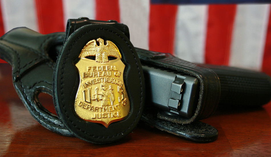 FBI badge and gun sitting on a table in front of the U.S. flag.
