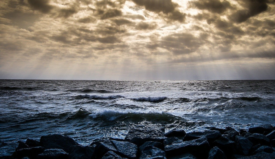 Ocean waves crash against a rocky shore under ominous clouds.