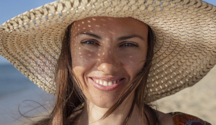 Smiling woman wearing a hat at the beach.