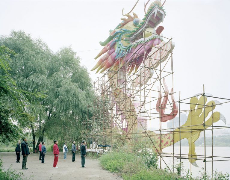 A group of people exercising under a dragon sign in Gansu Province.