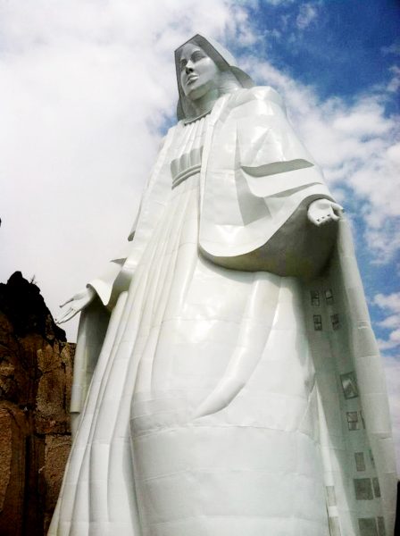 virgin mary statue of rocky mountains taken from the base of statue looking up with blue sky background and some white clouds