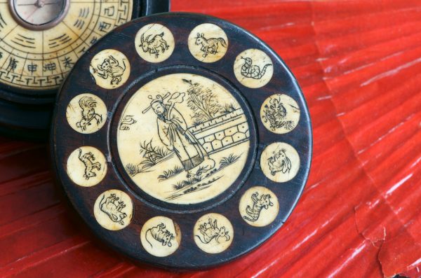 Antique Chinese Zodiac Wheel with feng shui compass made of engraved bone and wood on red fan background