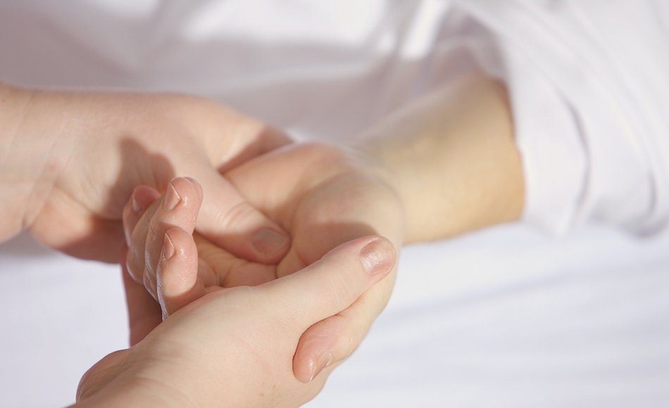 A pair of hands have another persons hand in theirs, detail of her white clothing is seen.