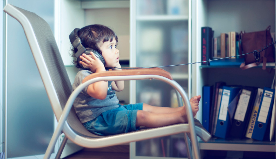 a toddler sits in a chair listening to music through headphones.
