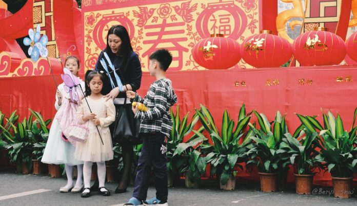 A Hong Kong mother stands with her boy and two girls who are holding whirligigs.