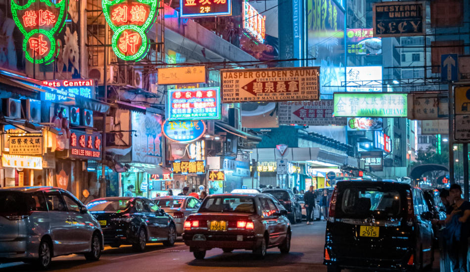 Hong Kong street at night, with traffic and lit shop signs.