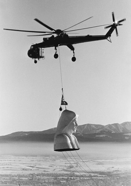black and white photo from 1985 of helicopter carrying large virgin mary head in the air