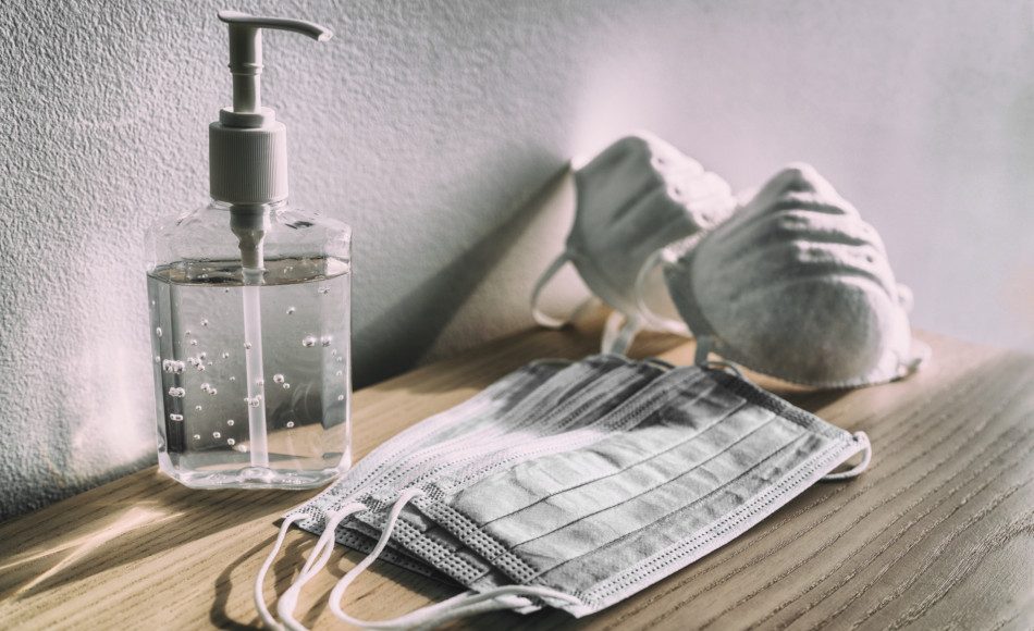 Hand sanitizer sits on a counter along with 2 types of masks.