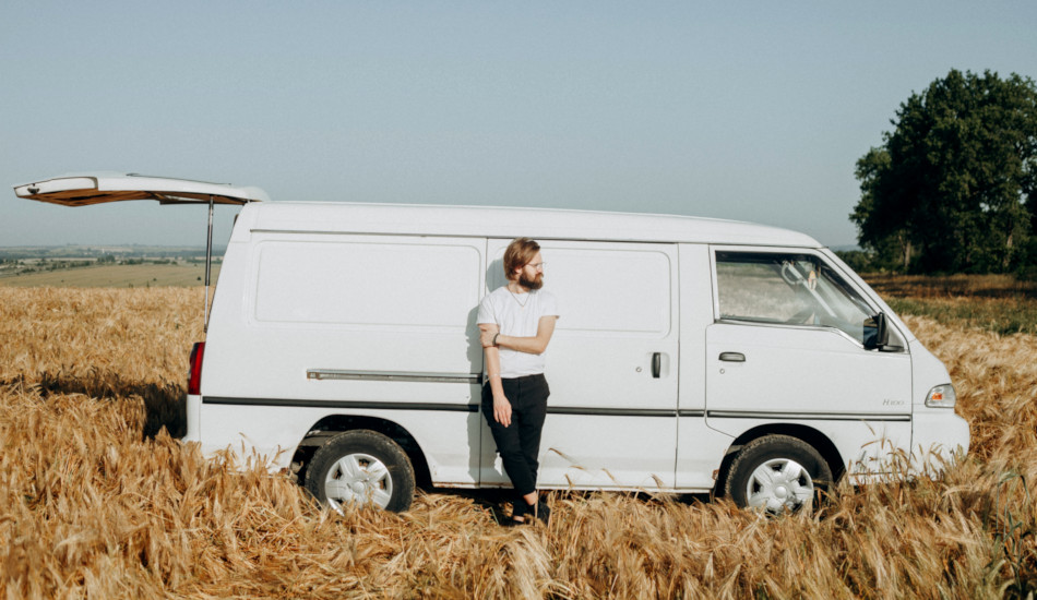 A man leaning against a white van parked in a wheat field.