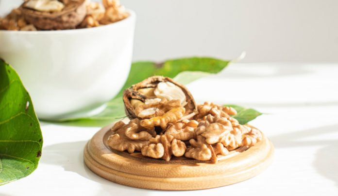 Walnuts sitting on a round board in front of a white bowl filled with nuts.
