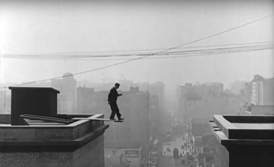 Buster Keaton walking on a plank on a high rise building with city in background