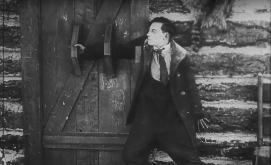 Buster Keaton with hand through door handles to secure a door (normally a big piece of wood would be in it's place)