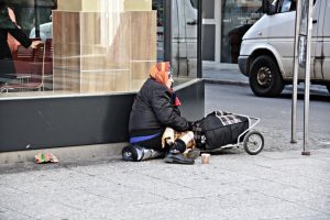 Homeless lady sitting with a trolley and warm jacket on the sidewalk.