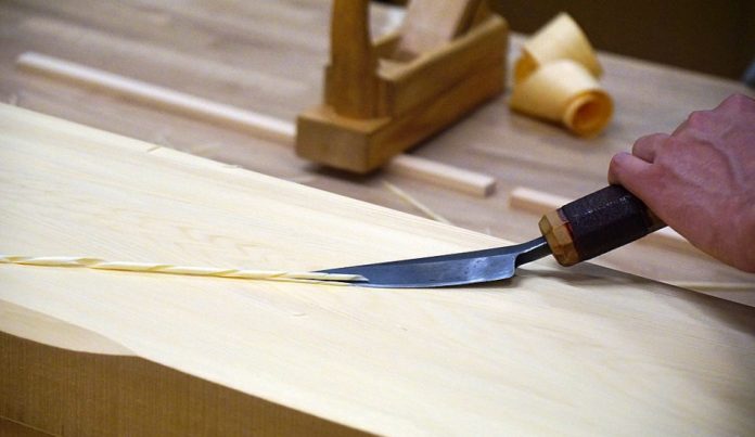 A man shaping a beam with woodworking tools.