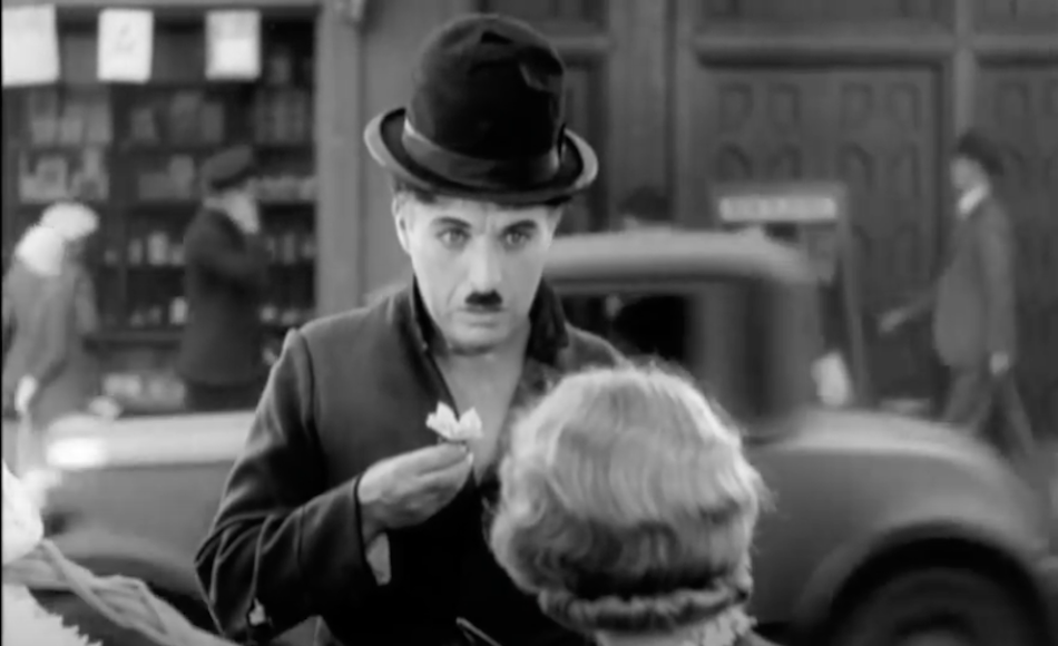 Charlie Chaplin holds a white flower about to hand to a lady