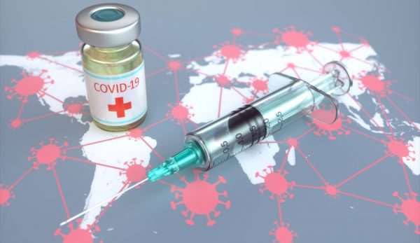 A vial and syringe sit atop a world map with the coronavirus drawn on it.