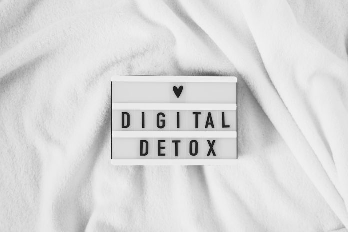 words spelling 'digital detox' and a black love heart on a light box that sits on a white blanket