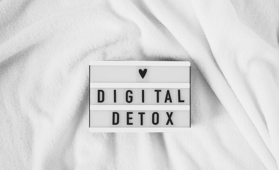 words spelling 'digital detox' and a black love heart on a light box that sits on a white blanket