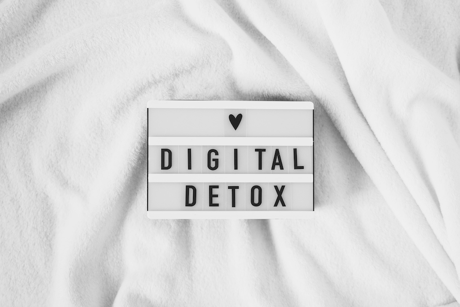words spelling 'digital detox' and a black love heart on a light box that sits on a white blanket