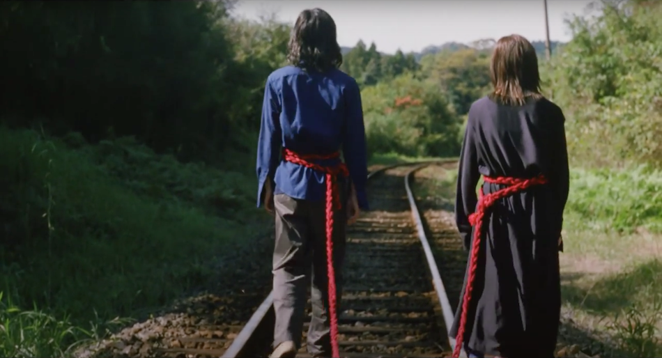 japanese couple walk along a railway track a red rope tied around each persons waist joining them together