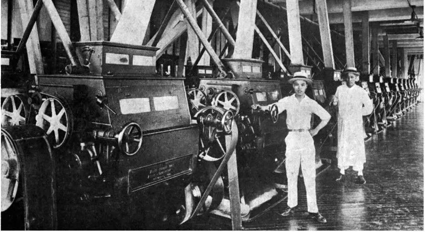 Machinery in the Rong Enterprises flour mill with two workers standing by.