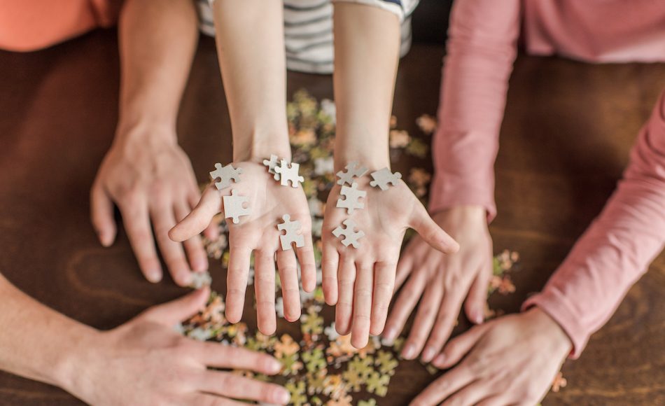 family with one child playing with puzzle on table we see hands only
