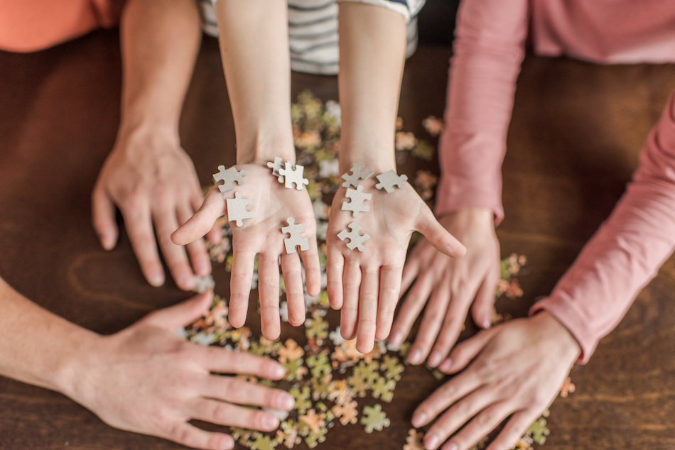 family with one child playing with puzzle on table we see hands only