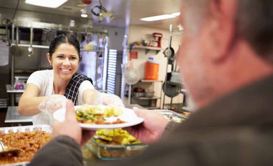 cheerful lady serves homeless man a plate of food