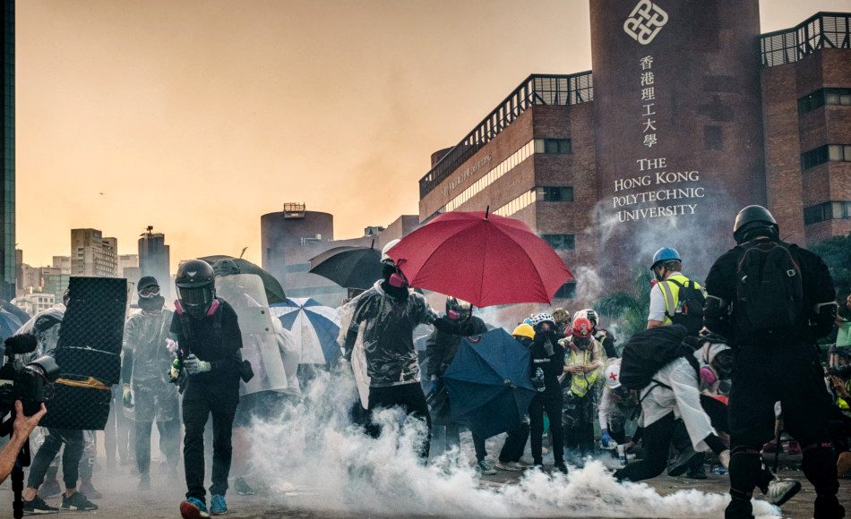Students in face masks with umbrellas along with medical aid workers stand amidst tear gas canisters lobbed at them by police in front of Hong Kong Polytechnic University on November 17, 2019.