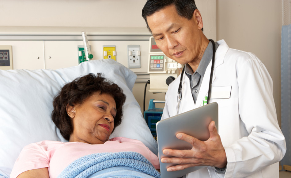 A male doctor confers with a female patient laying in a hospital bed.