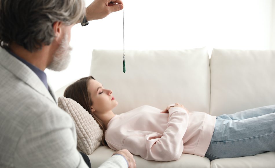lady lying on therapist couch with eyes closed therapist holds pendulum above her