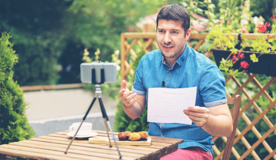 A man sits in front of a smartphone on a tripod, participating in a videoconference.