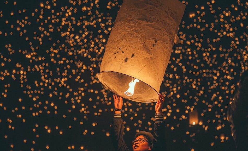 person releasing sky lantern into sky with many lit up behind her, we can see she has written what she wishes for in the New Year on the lantern.