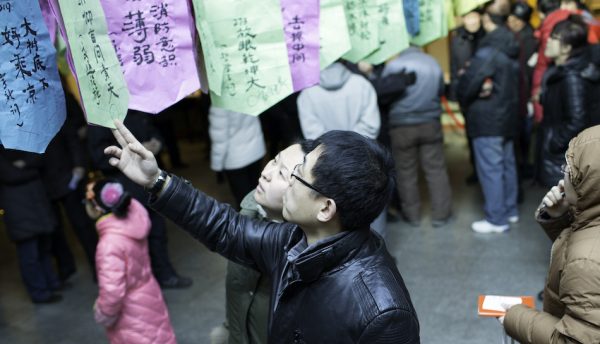 chinese couple look at riddles written on paper hanging up high, part of a tradition in the chinese lantern festival