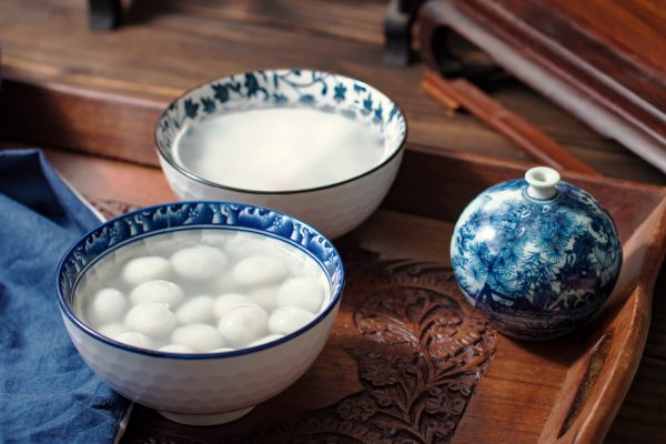 sticky rice balls in blue and white porcelain bowl with dark wood carved table and furniture in background.
