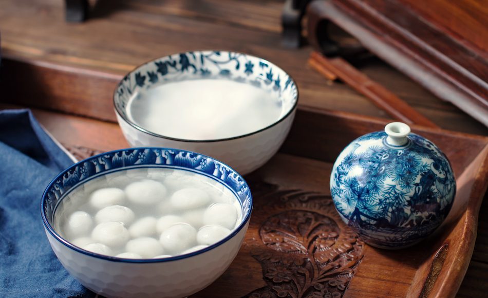 sticky rice balls in blue and white porcelain bowl with dark wood carved table and furniture in background.